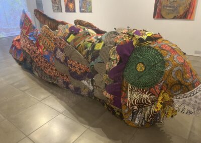 The Nightjar sculpture in a gallery, surrounded by paintings by Kwame that reflect stories from migrants.