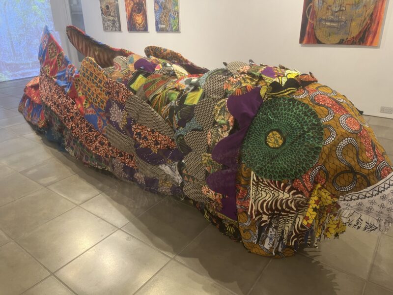 Nightjar: A sculpture woven from New Forest willow, wrapped in Ankara fabric, and inspired by Ghanaian bird-catcher cages. Hanging birds made from milk bottles and migrant-story paintings complete this powerful fusion of heritage, craft, and community.